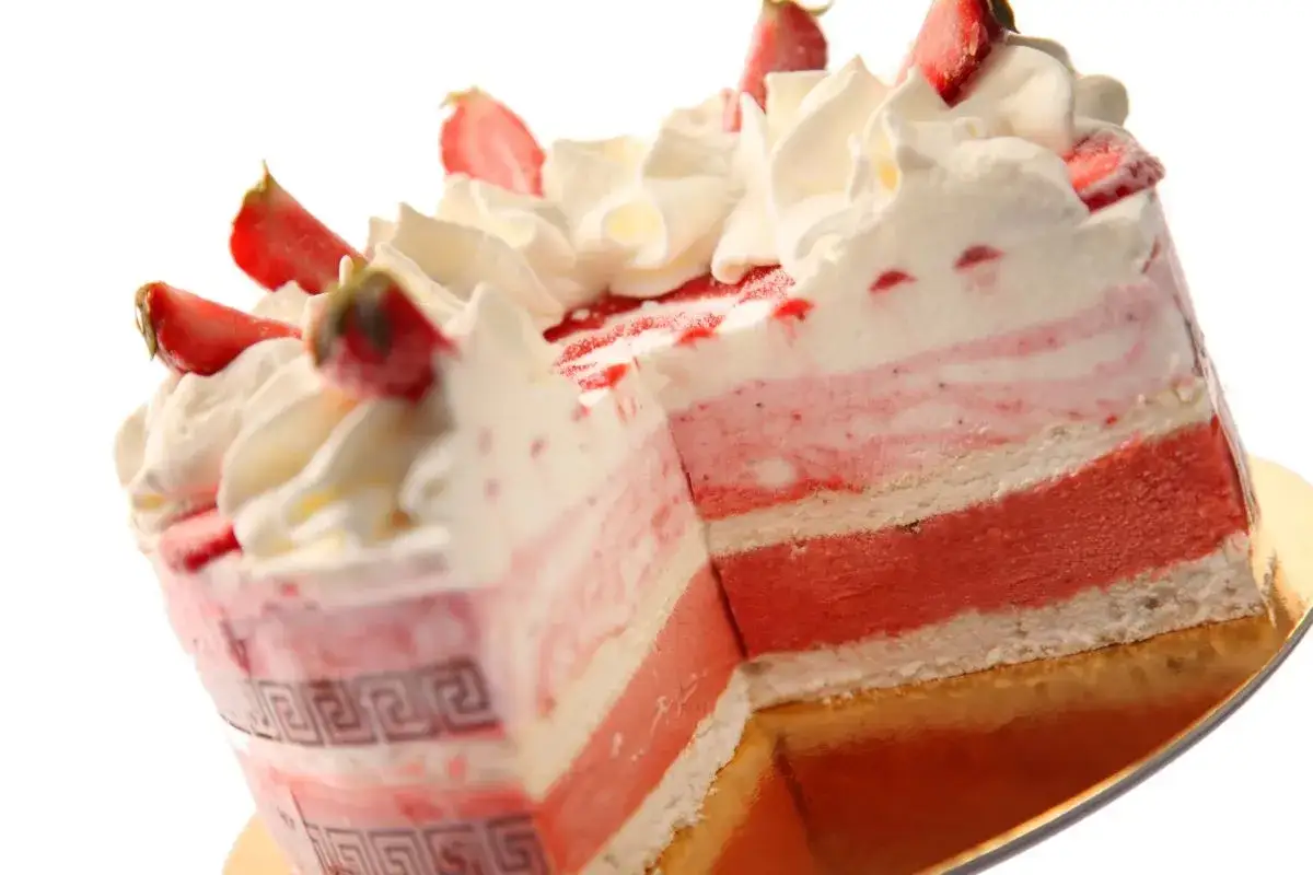 Tort lodowy z warstwami truskawkowymi, bitą śmietaną i kawałkami truskawek.