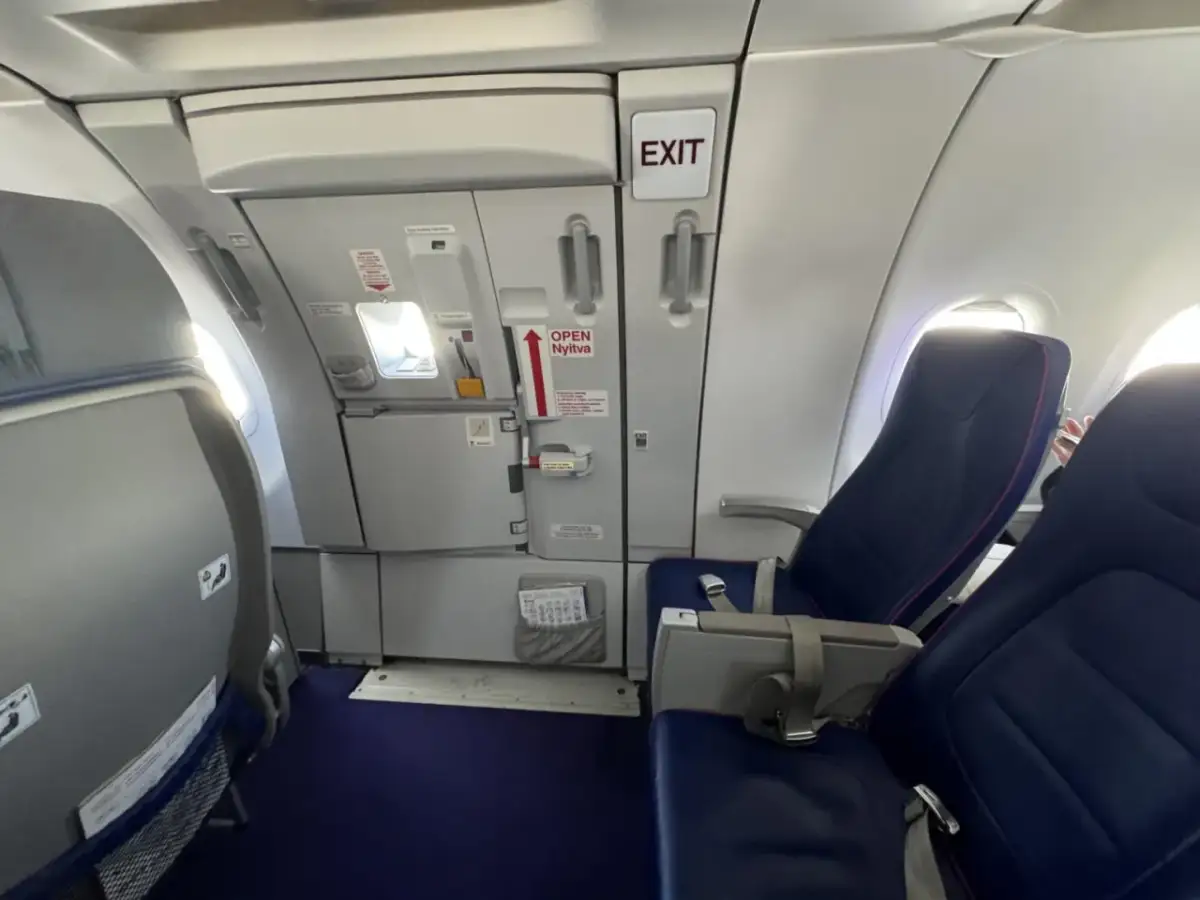 Wnętrze samolotu Wizzair. Widok na rząd siedzeń i drzwi wyjściowe. Numeracja miejsc w samolocie Wizzair jest widoczna na siedzeniach.