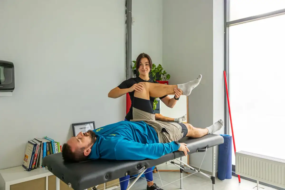 Fizjoterapeuta wykonuje ćwiczenie z pacjentem leżącym na kozetce.