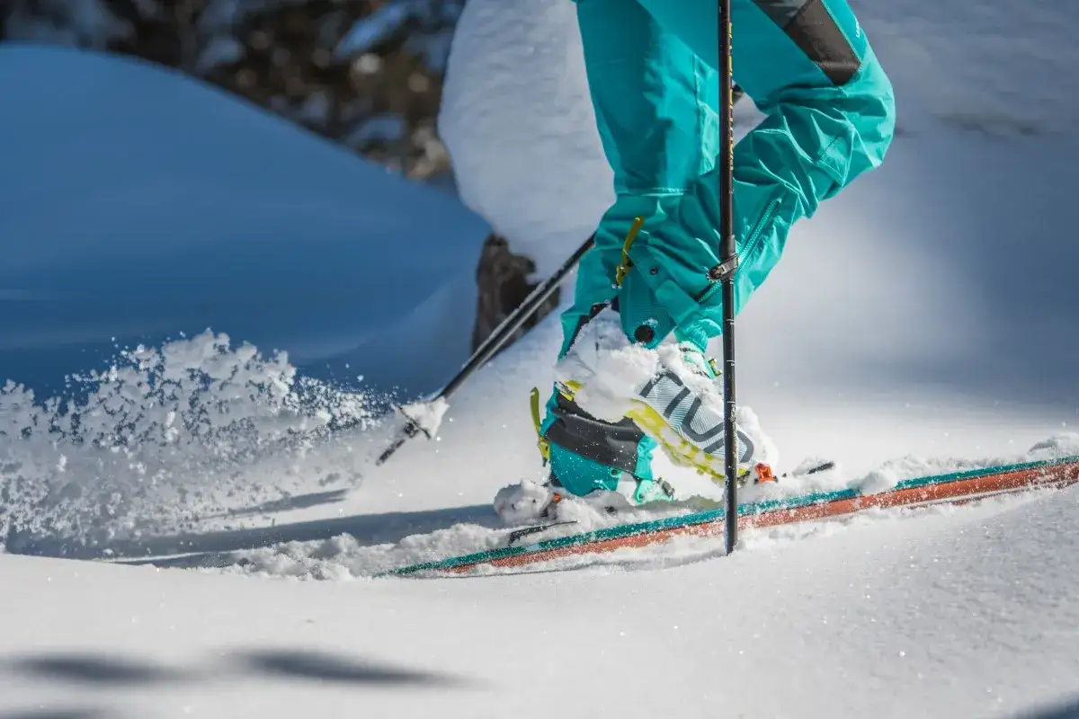Narciarz w turkusowych spodniach i butach z rakami automatycznymi lub półautomatycznymi przemierza ośnieżone stoki.