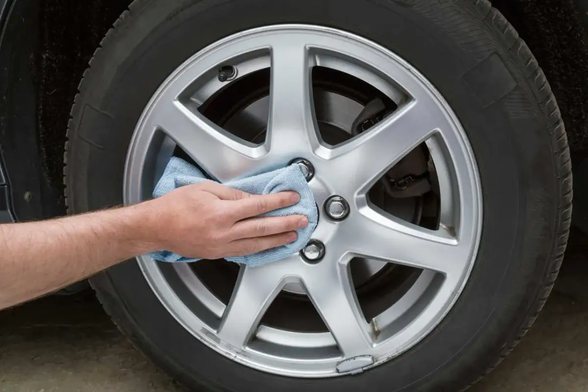 Dłoń z niebieską ściereczką poleruje felgi aluminiowe, przywracając im blask.