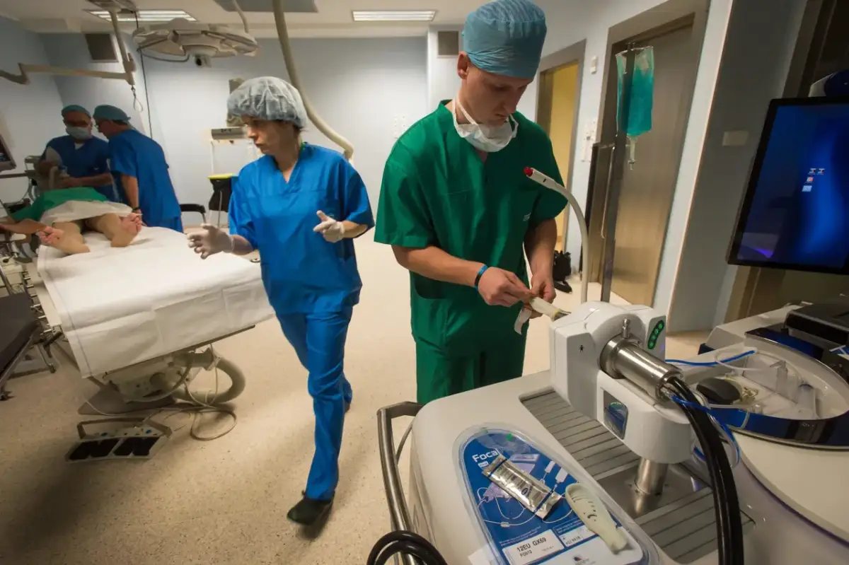 Chirurdzy w zielonych i niebieskich fartuchach w sali operacyjnej, przygotowujący pacjenta.