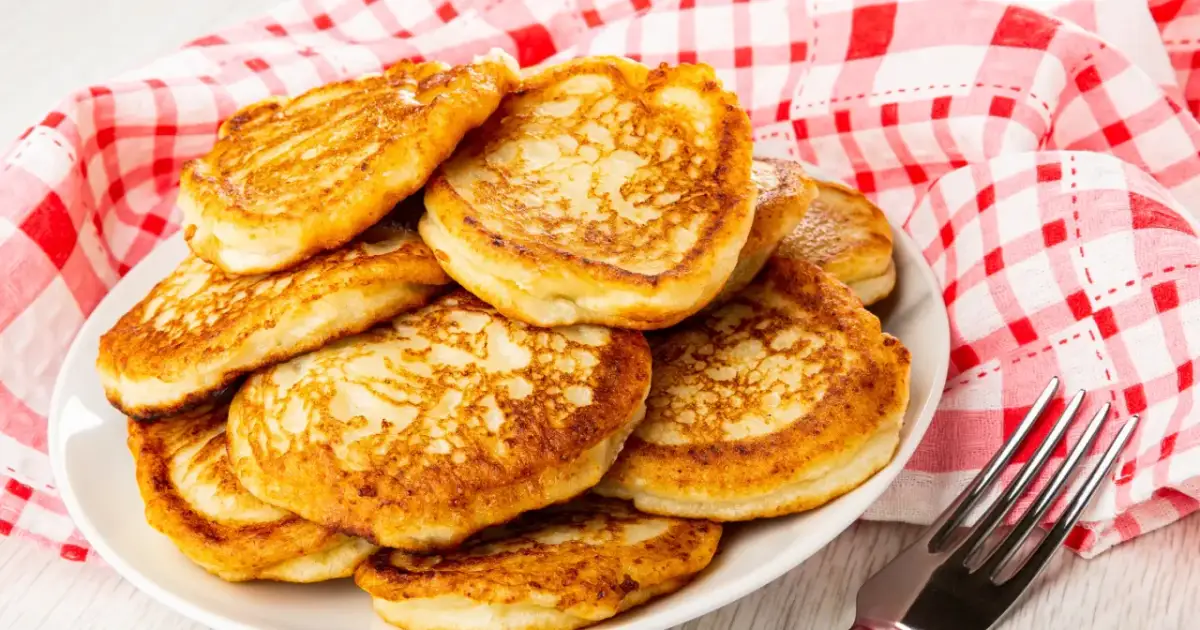 Złociste placuszki z serka wiejskiego fit, ułożone na białym talerzu, obok czerwono-białej serwetki. Idealne na lekki posiłek.