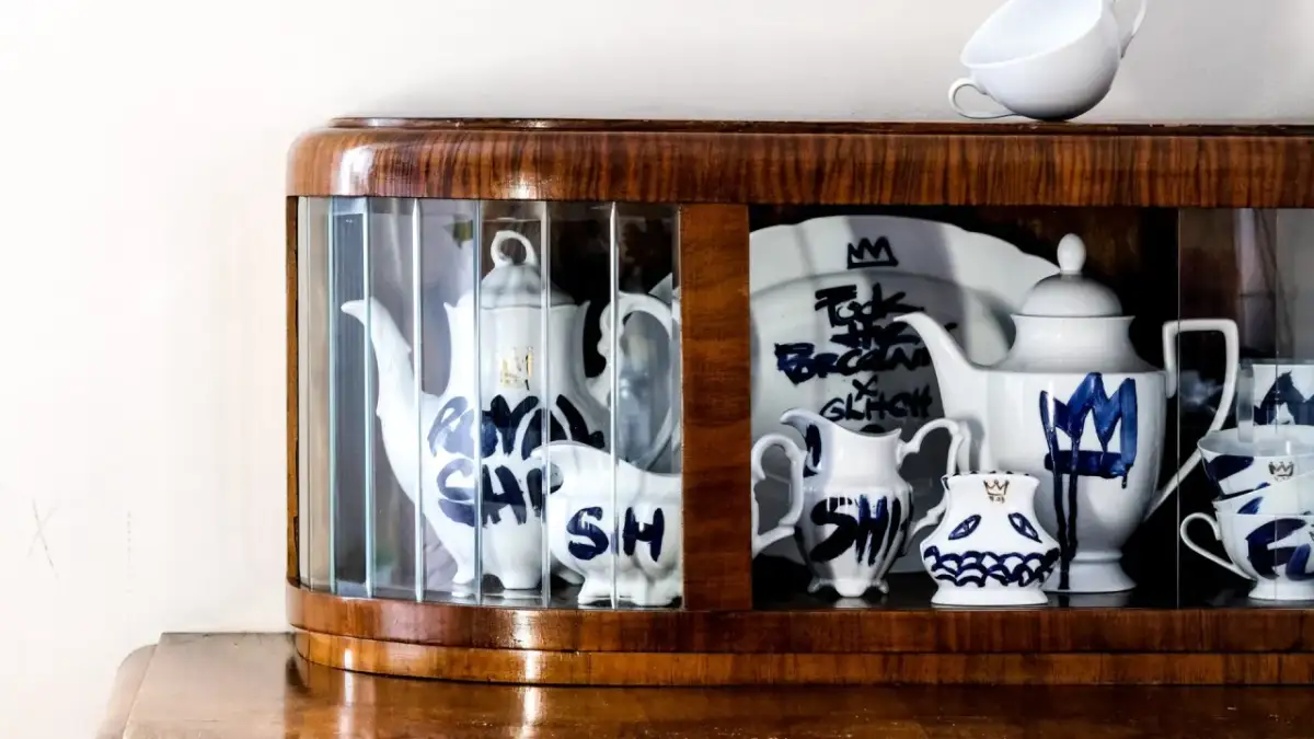 W gablocie z drewna i szkła stoją białe naczynia, jakby z piosenki o porcelanie, ozdobione niebieskimi wzorami i napisami.