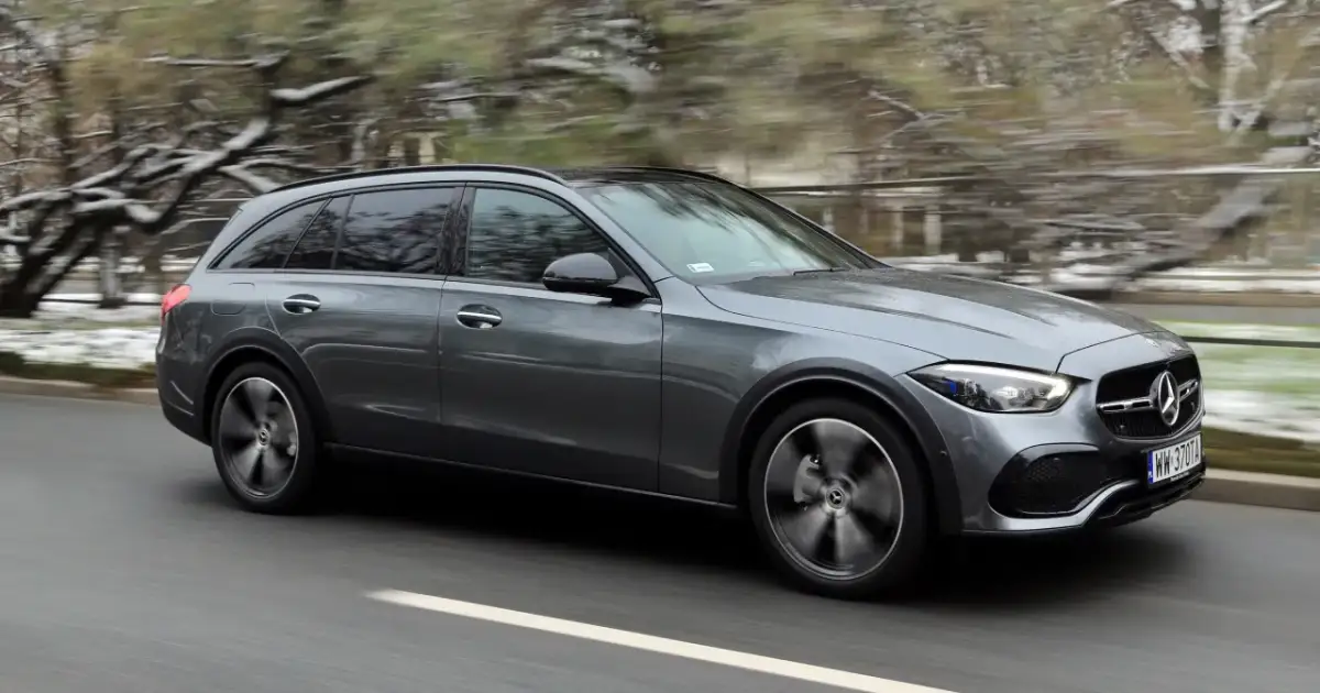 Szary Mercedes All-Terrain z napędem 4matic pędzi po drodze, zaśnieżone drzewa w tle.