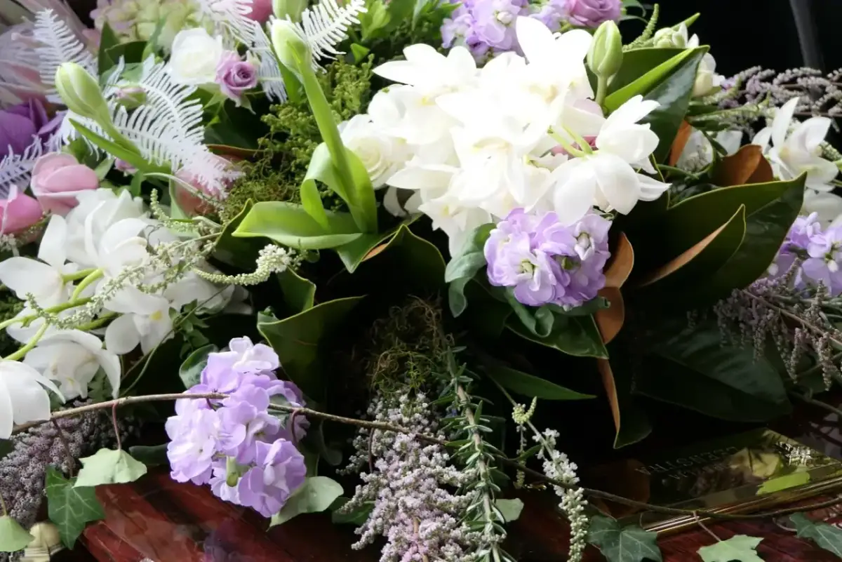 Wiązanka pogrzebowa z białych i fioletowych kwiatów, zielonych liści i paproci.