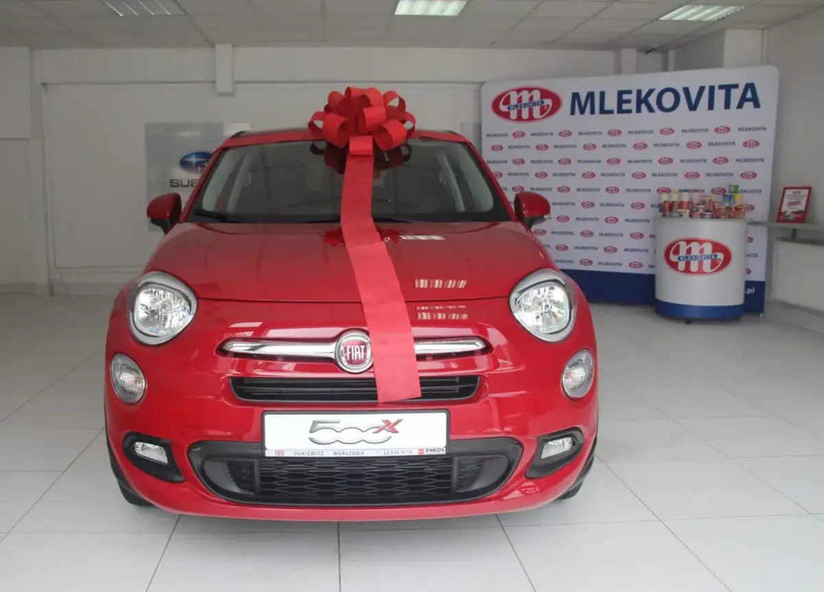 Czerwony Fiat 500X z wielką czerwoną kokardą, gotowy do wręczenia jako nagroda w loterii promocyjnej Vitay.
