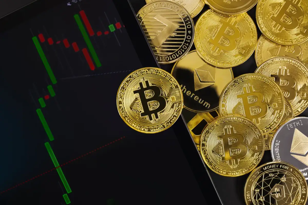 Złote monety kryptowalut obok wykresu świecowego. Dowiedz się, jak rozliczać kryptowaluty, analizując dane rynkowe.