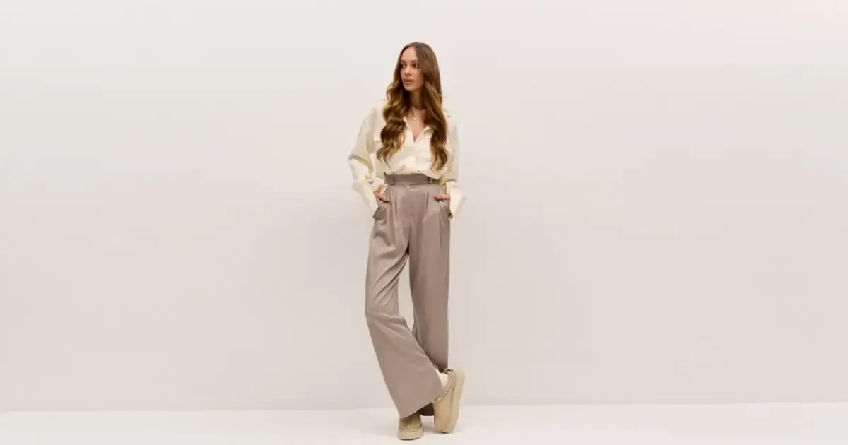 Młoda kobieta w eleganckim, beżowym zestawie: luźna koszula i szerokie spodnie.