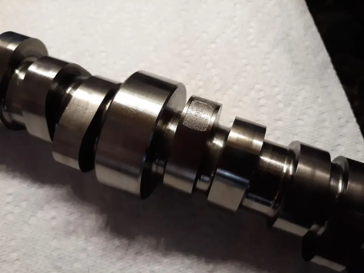 Metalowy wałek rozrządu z widocznymi śladami zużycia, wskazującymi na potencjalne objawy awarii.