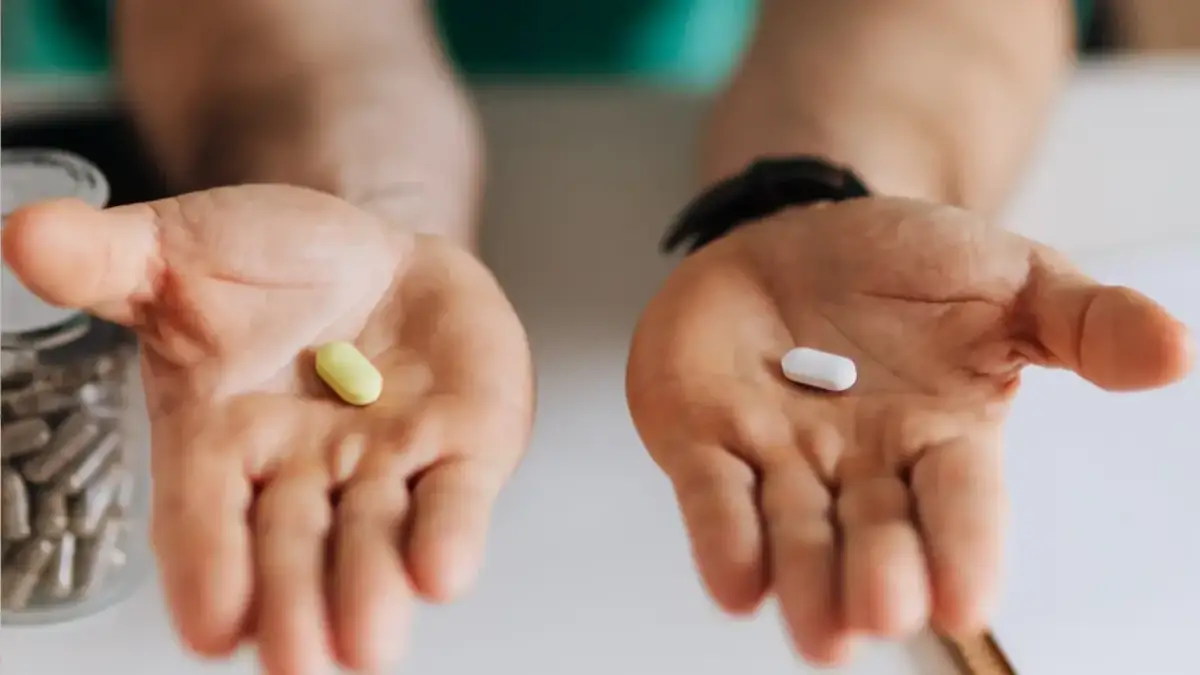 Dwie dłonie, jedna z żółtą tabletką, druga z białą. Apap czy Ibuprom – dylemat bólu głowy.