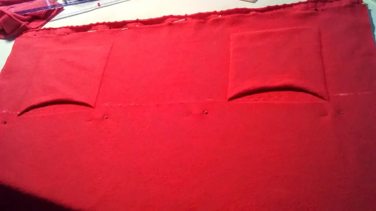 Czerwony materiał, przygotowany do szycia, z zaznaczonymi kieszeniami. Może to być etap pracy nad tym, jak zmniejszyć sweter, by idealnie pasował.