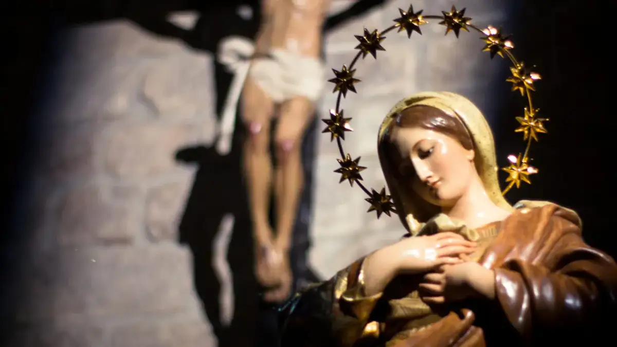 Figurka Matki Bożej z gwiazdami na głowie, w tle ukrzyżowany Jezus. Symbol bólu i cierpienia, jak w różańcu części bolesne.
