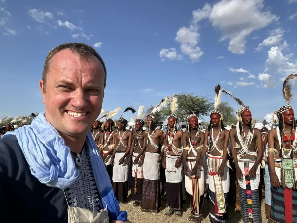 Rafał Banaś na tle grupy mężczyzn w tradycyjnych strojach i makijażu.