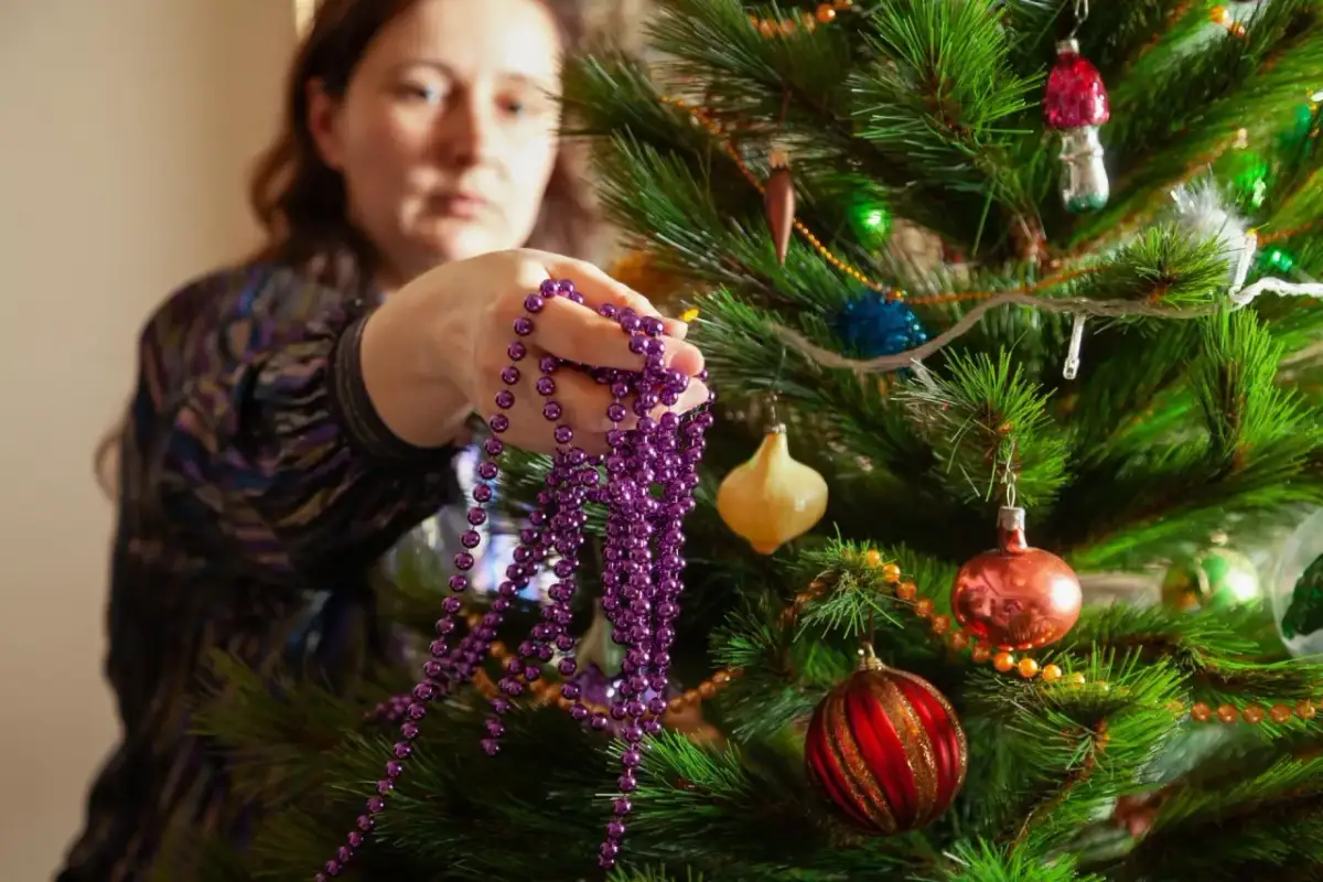 Kiedy ściągamy ozdoby świąteczne, kobieta trzyma fioletowy sznur koralików przy choince z bombkami.