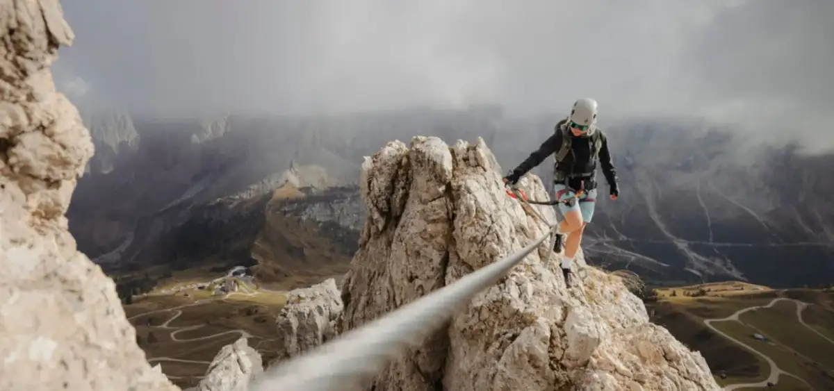 Kobieta w kasku i uprzęży pokonuje via ferrata, czyli ubezpieczoną trasę w skałach. Widok zapiera dech w piersiach.