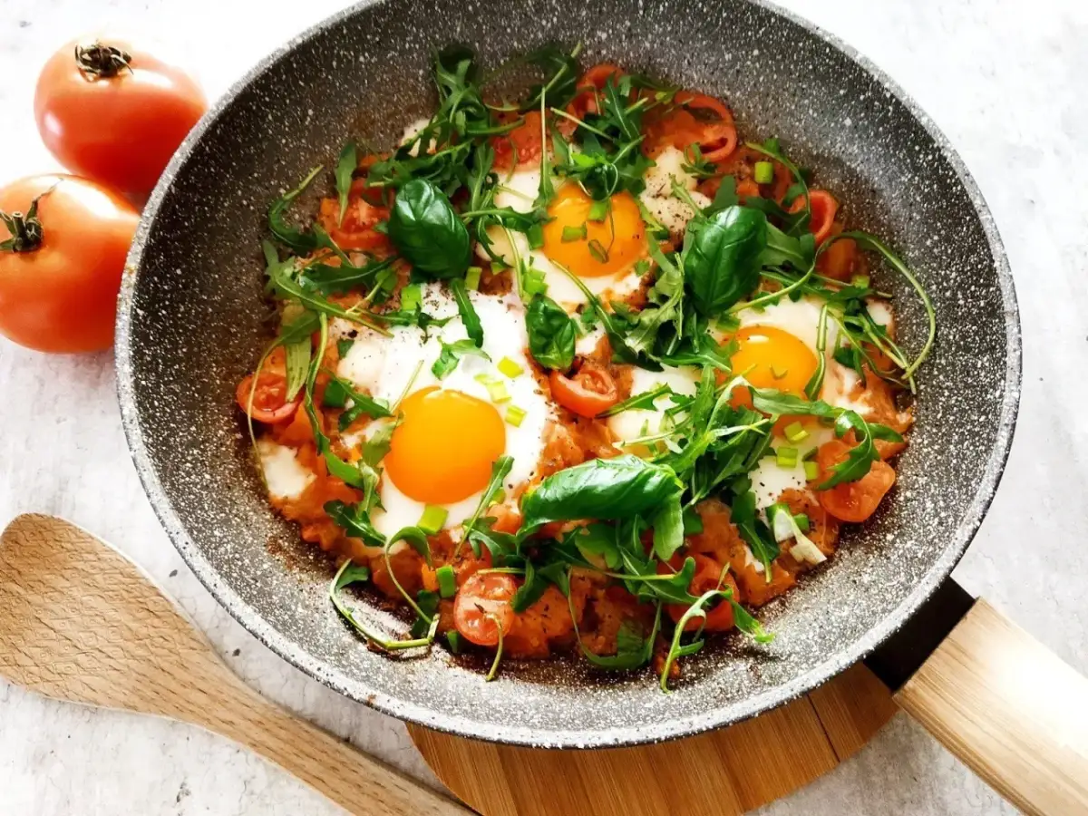 Jajka sadzone z pomidorami, rukolą i bazylią na patelni.