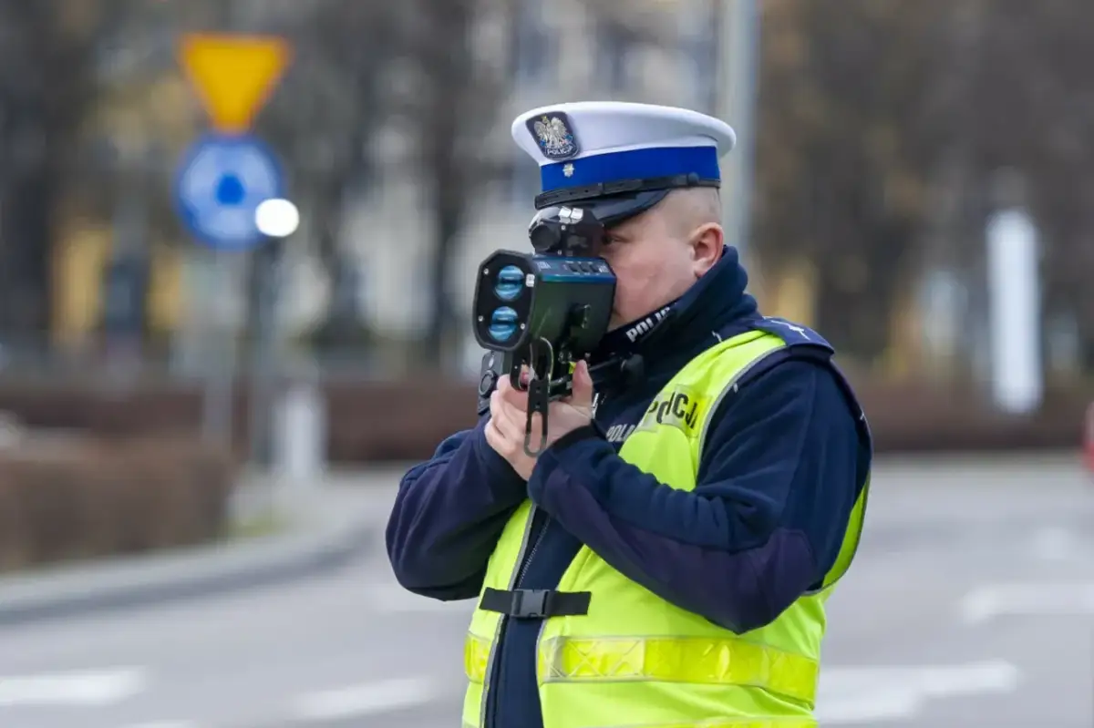 Policjant w kamizelce odblaskowej mierzy prędkość pojazdu. Uważaj na przekroczenie prędkości!