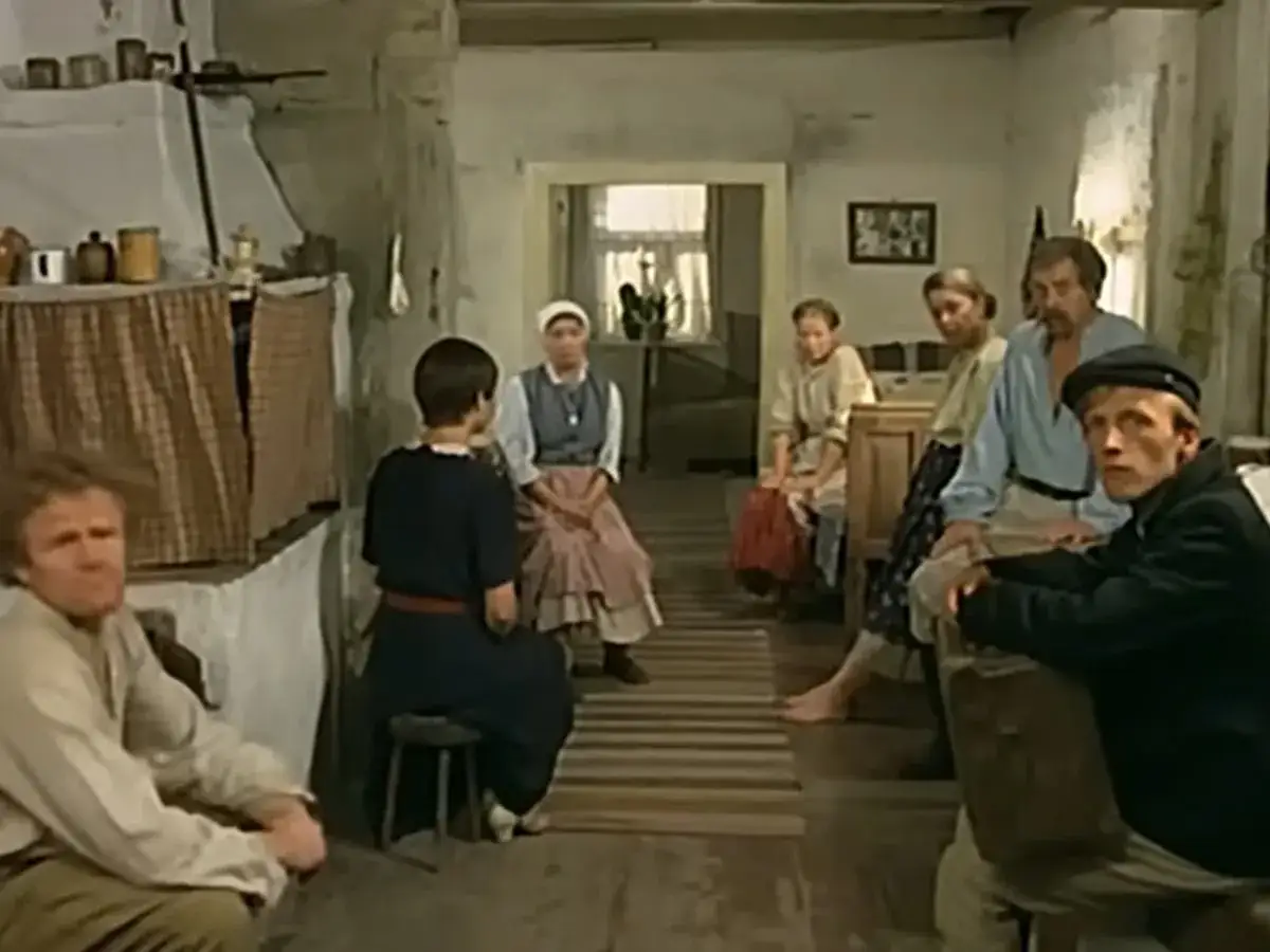 Scena z filmu "Znachor", gdzie nagrywali w wiejskiej chacie. Ludzie siedzą w skromnym wnętrzu, czekając na pomoc.