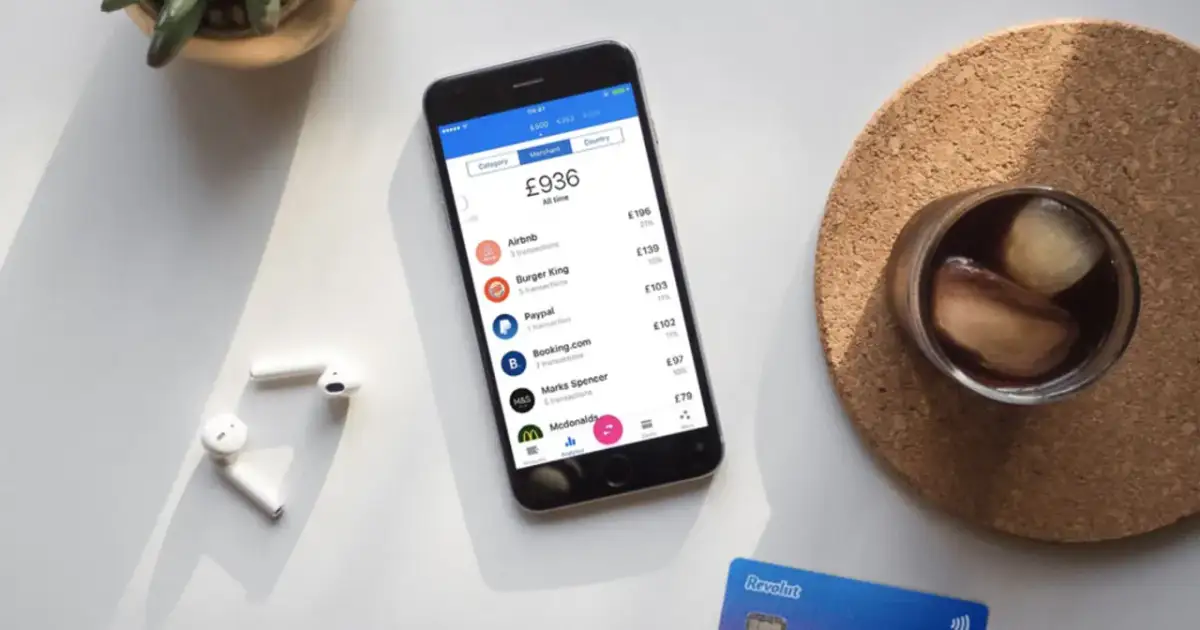 Telefon z aplikacją Revolut pokazuje transakcje, ułatwiając zrozumienie, jak płacić Revolutem za granicą. Obok leżą słuchawki i karta.