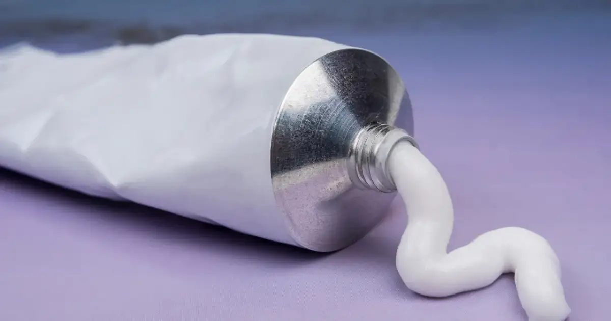 Biała pasta wydobywa się z metalowej tubki. To może być krem z witaminą F na co dzień, dla zdrowej skóry.