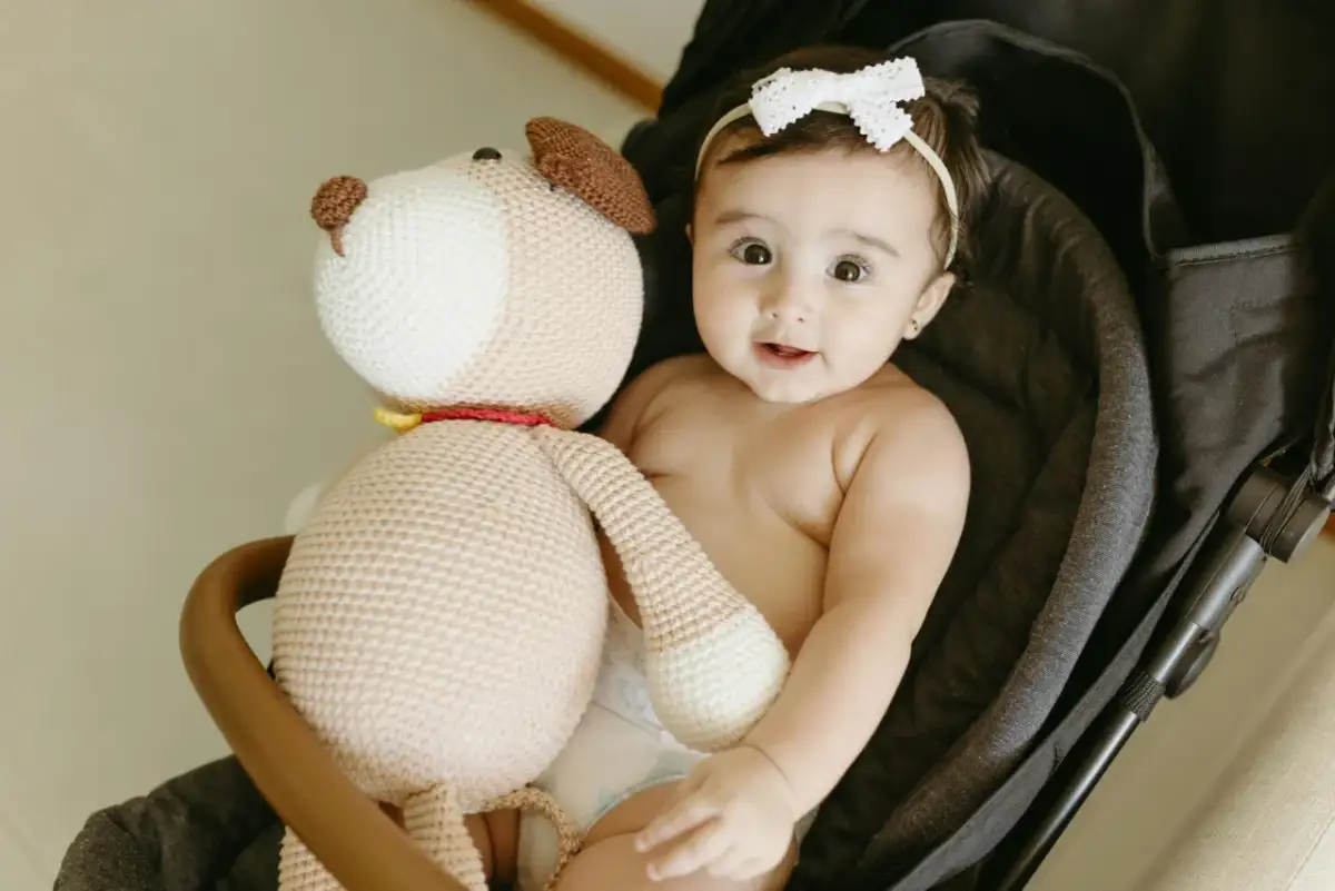 Uśmiechnięte dziecko w wózku z pluszowym pieskiem. Idealny moment, kiedy kompletować wyprawkę.