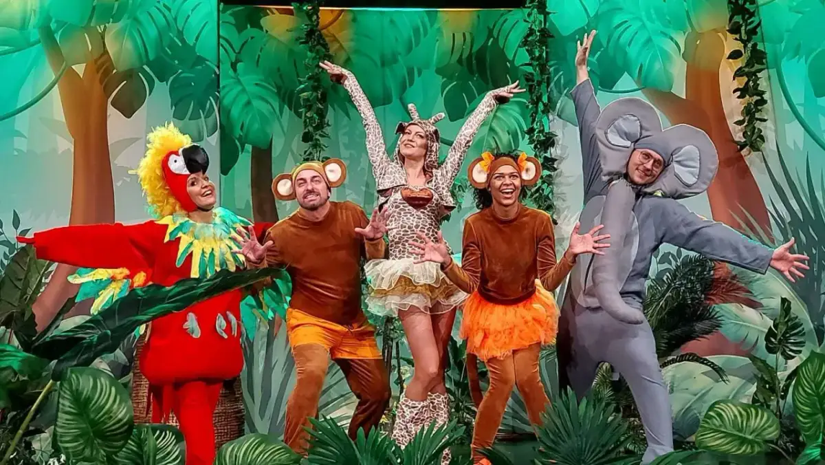 Zuzanna w stroju żyrafy i jej przyjaciele – papuga, małpki i słoń – bawią się na scenie podczas wesołego spektaklu.