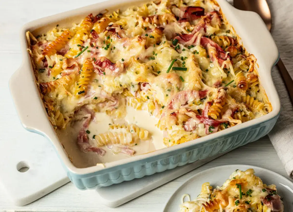 Pyszna zapiekanka makaronowa z szynką, pokryta ciągnącym się serem i posypana szczypiorkiem.