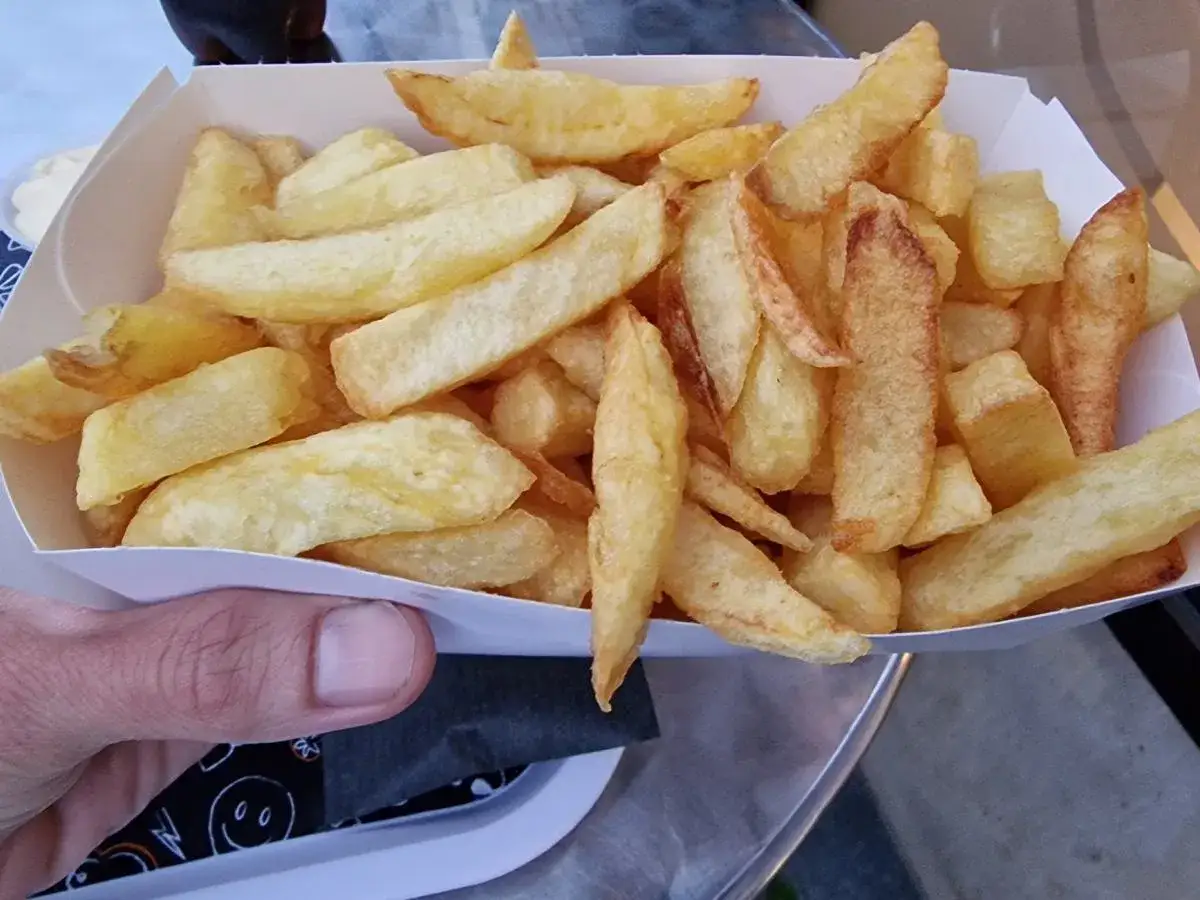 Złociste, chrupiące frytki w papierowym opakowaniu, trzymane w dłoni.