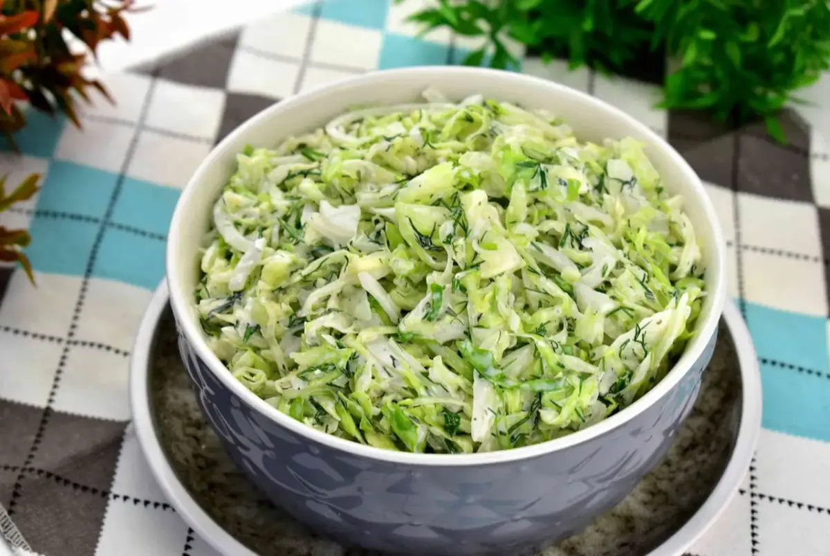 Pyszna surówka z białej kapusty z koperkiem, podana w szarej misce na wzorzystym obrusie.