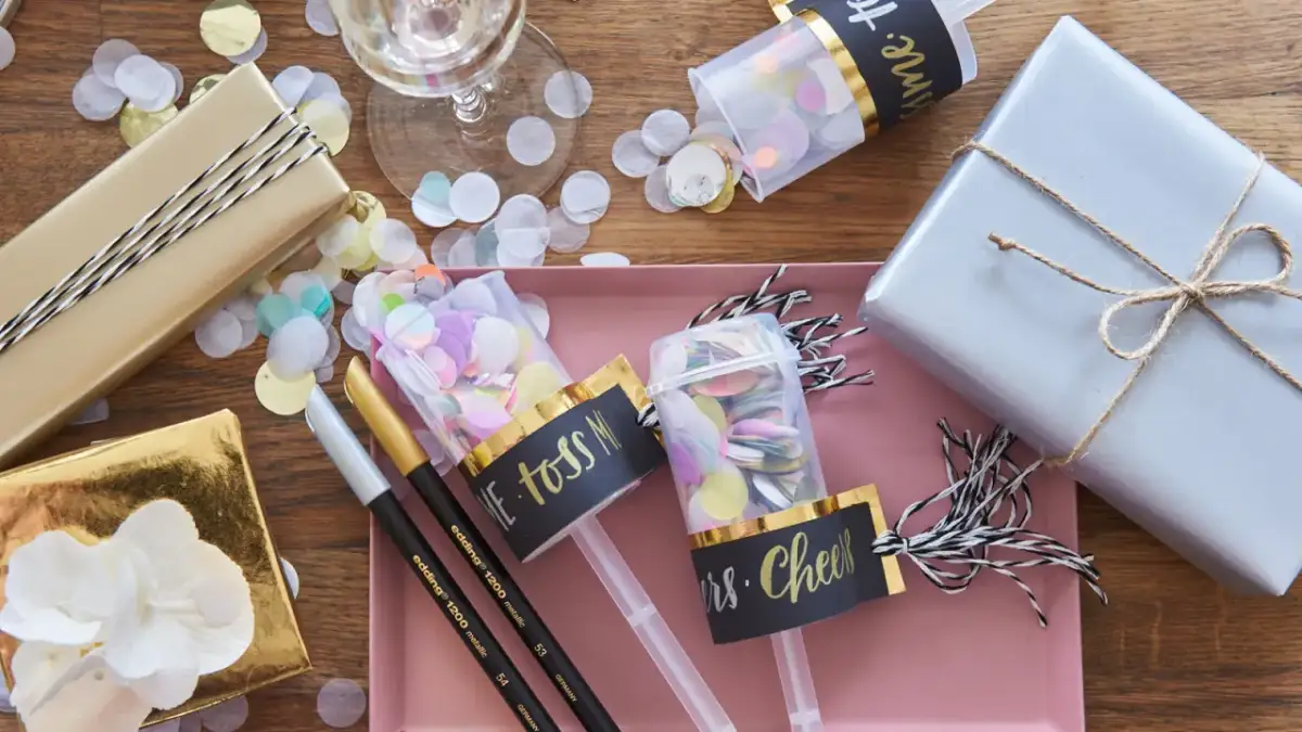 Złote i srebrne prezenty, konfetti, kieliszek i tuby strzelające z konfetti.