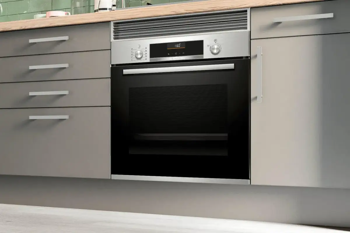 Moderno horno integrado en una cocina con cajones grises y encimera de madera.