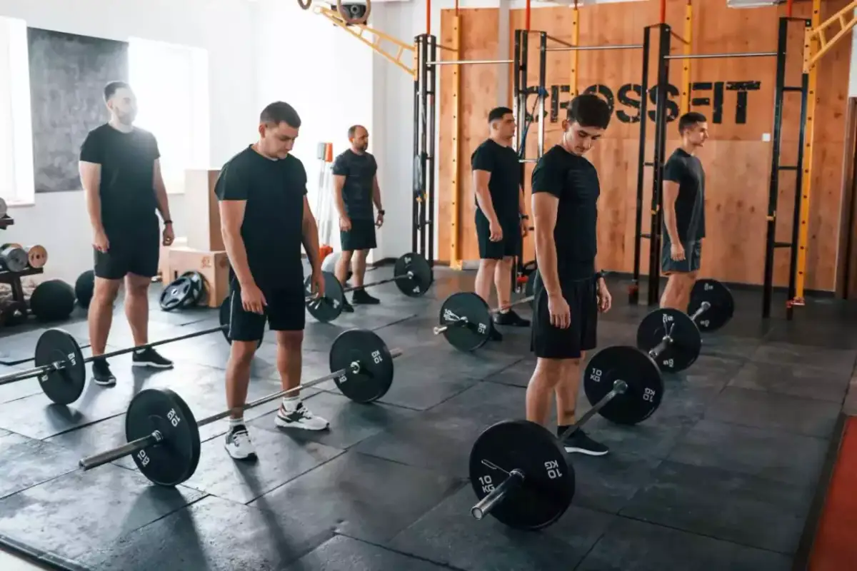 Mężczyźni w czarnych strojach ćwiczą z ciężarami w sali treningowej. Czy crossfit jest zdrowy? Ta grupa wydaje się to sprawdzać.