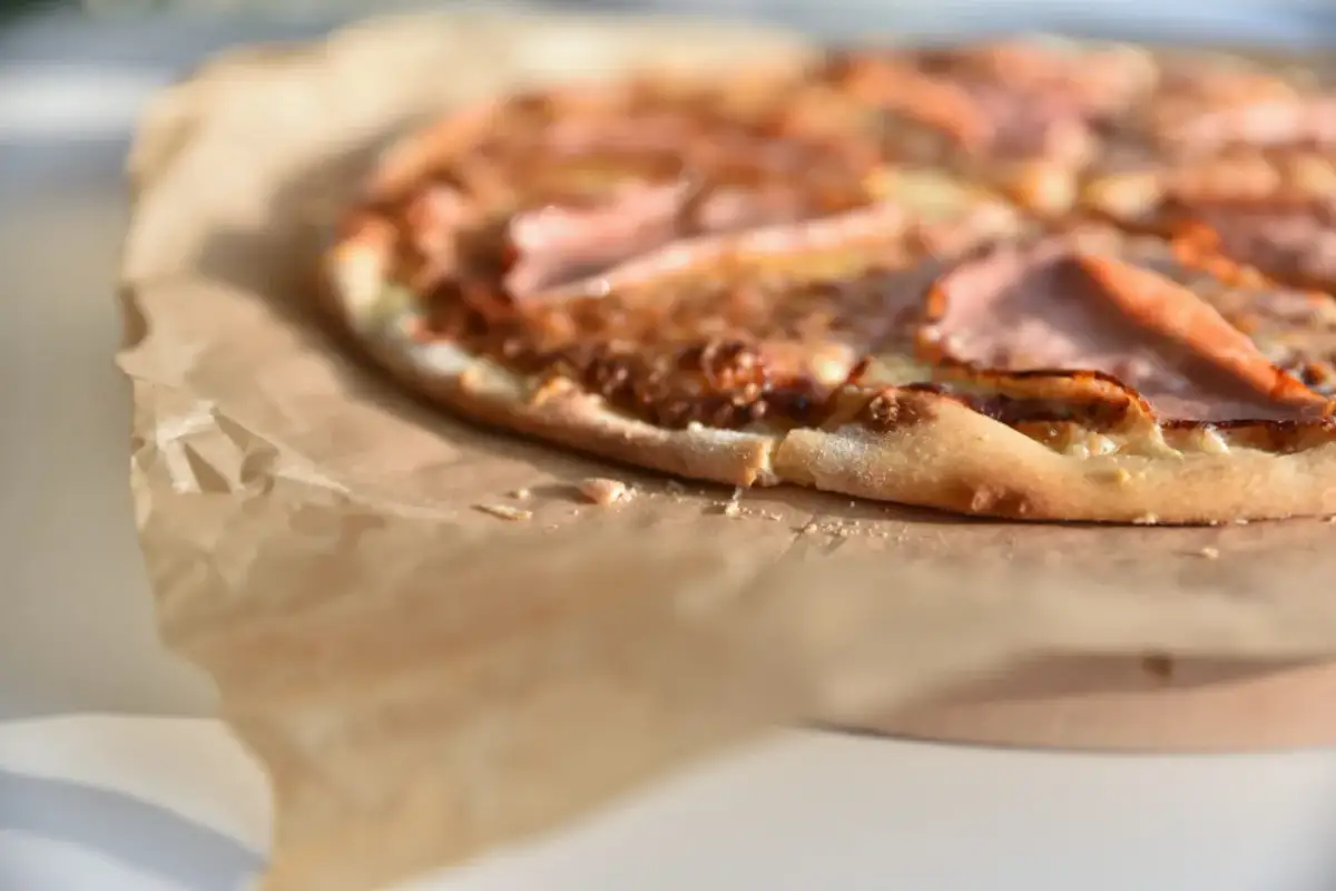 Fragment pizzy z szynką na papierze do pieczenia, z bliska, rozmyte tło.