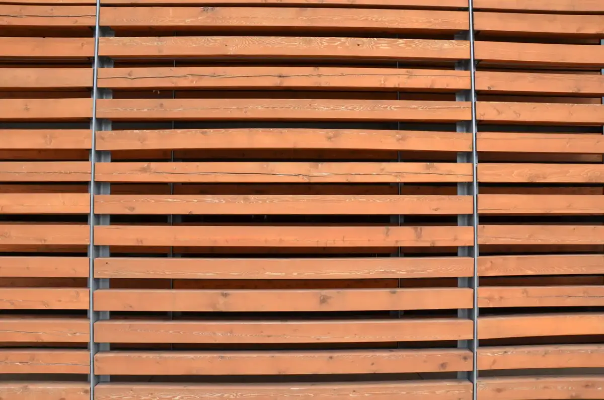 Drewniane lamele ścienne w kolorze miodowym, ułożone poziomo i przymocowane do szarych słupków.