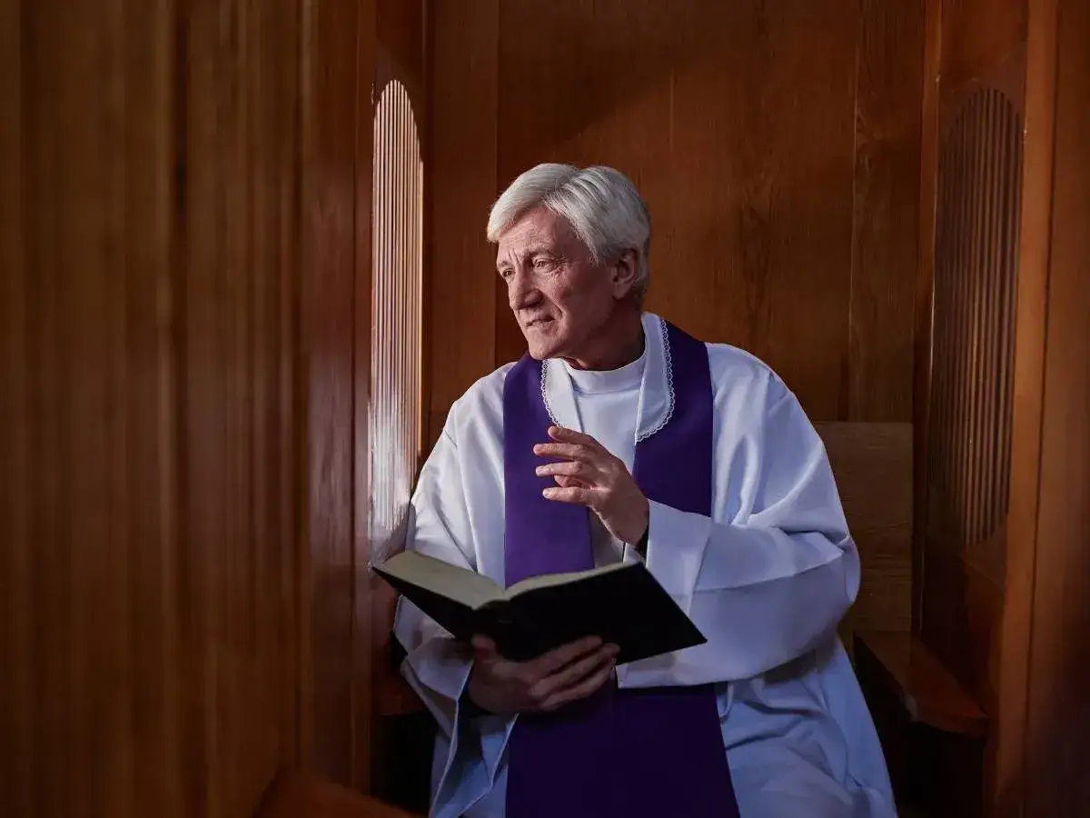 Kapłan w konfesjonale, z otwartą księgą, omawia warunki dobrej spowiedzi.