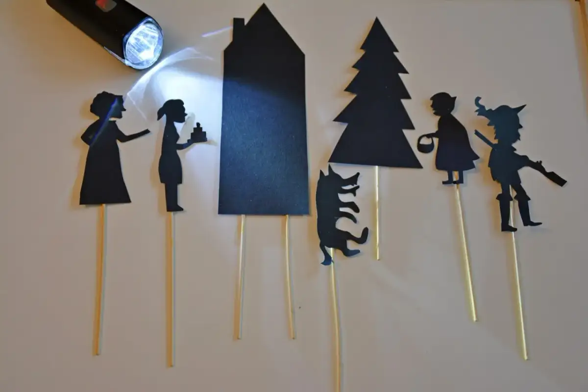 Jak zrobić teatrzyk cieni: wycinanki postaci i budynków na patyczkach, oświetlone latarką.