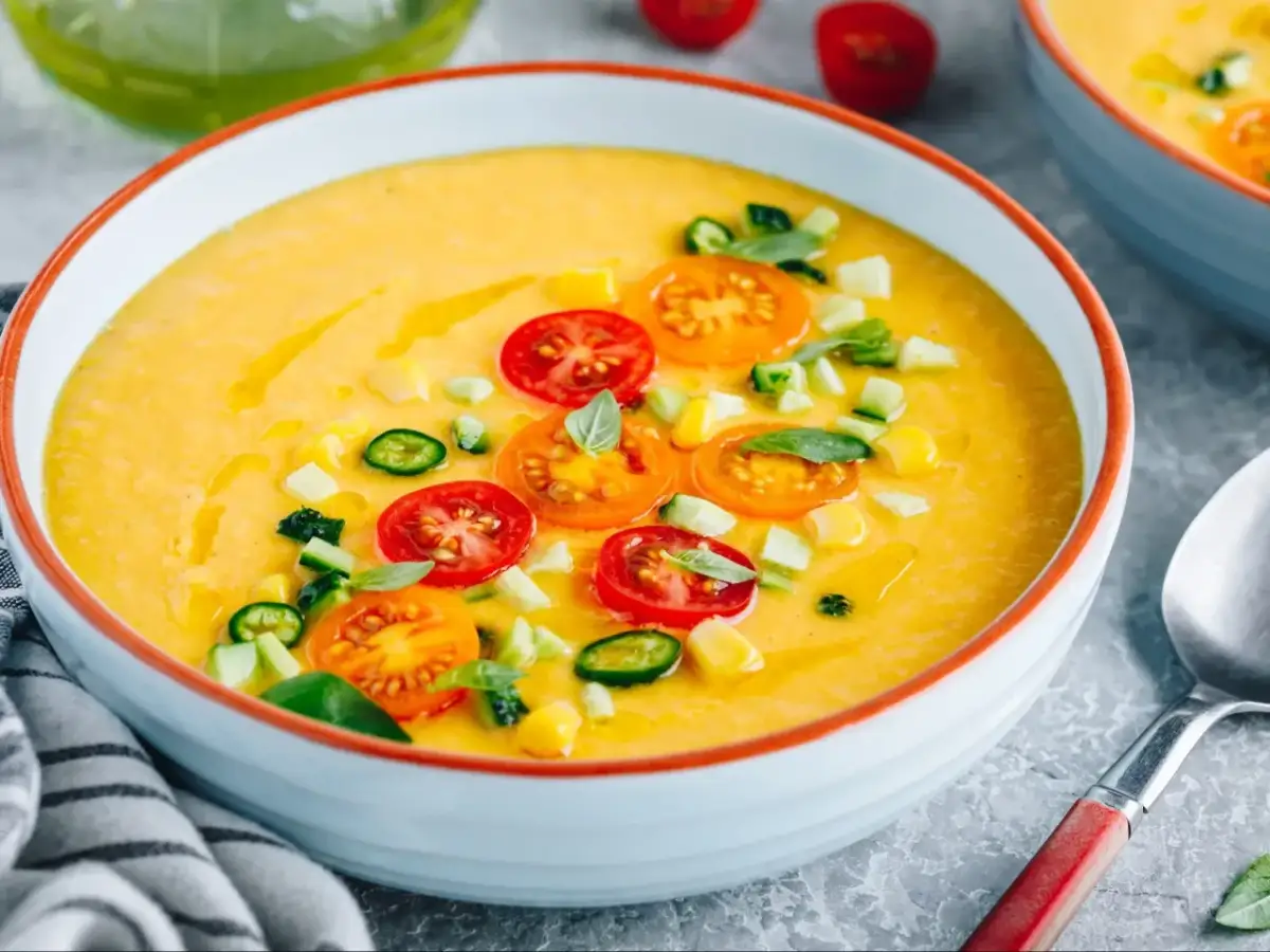 Chłodnik z pomidorów, ozdobiony plasterkami pomidorków, ogórka i kukurydzy, wygląda orzeźwiająco.