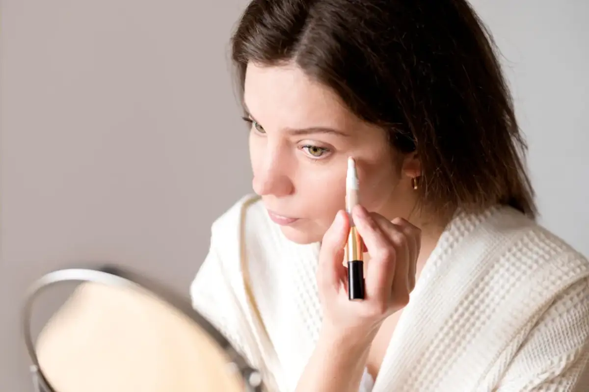 Kobieta aplikuje korektor pod oczy za pomocą pędzelka.