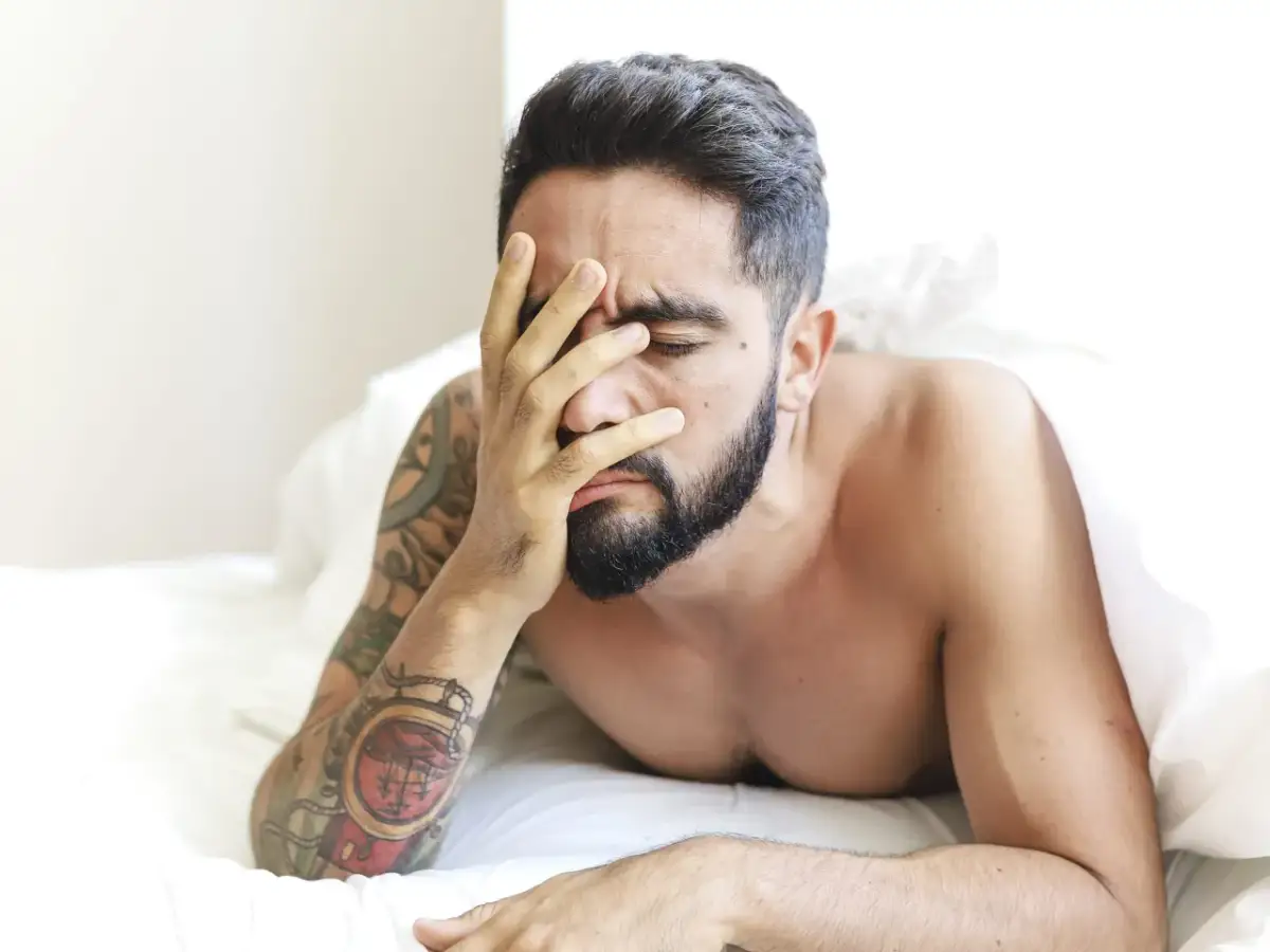 Mężczyzna z tatuażami na ramieniu, z ręką na twarzy, zastanawia się, w jakim wieku spada popęd seksualny u mężczyzn.