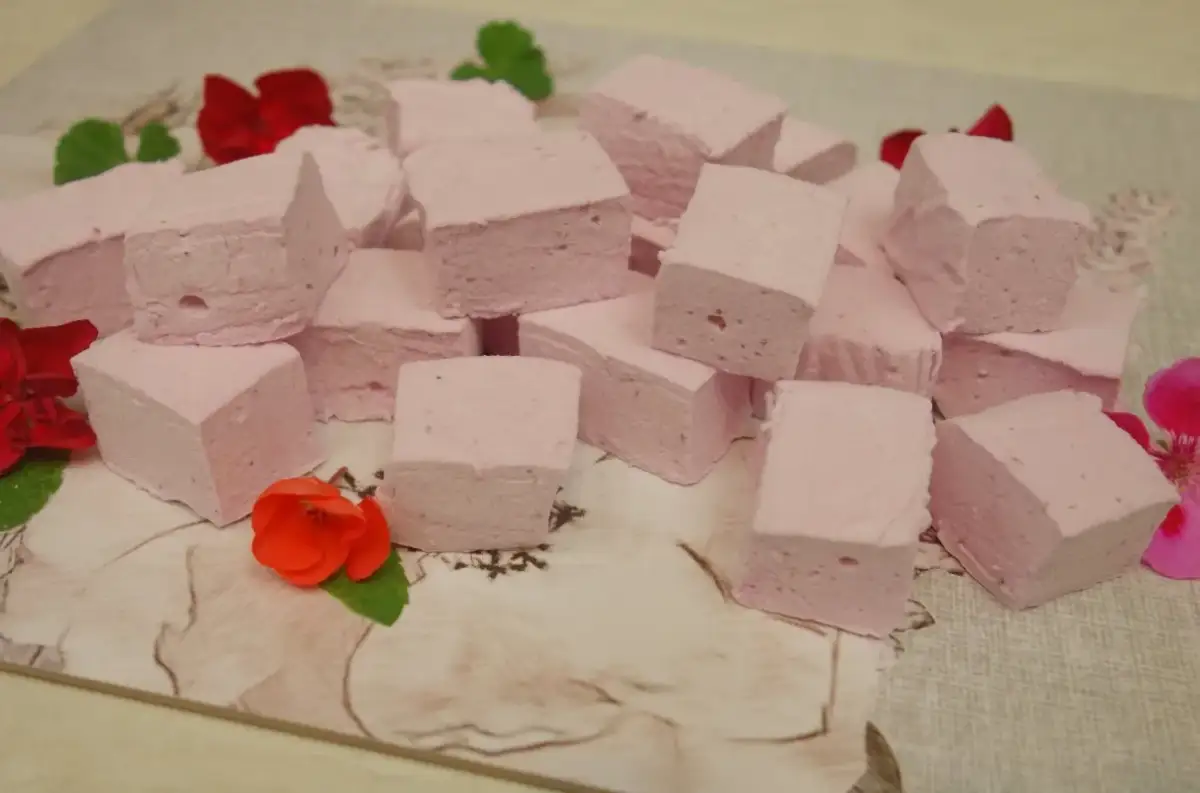 Różowe pianki marshmallow, idealne do domowego przepisu. Ułożone na wzorzystym tle, ozdobione kwiatami.