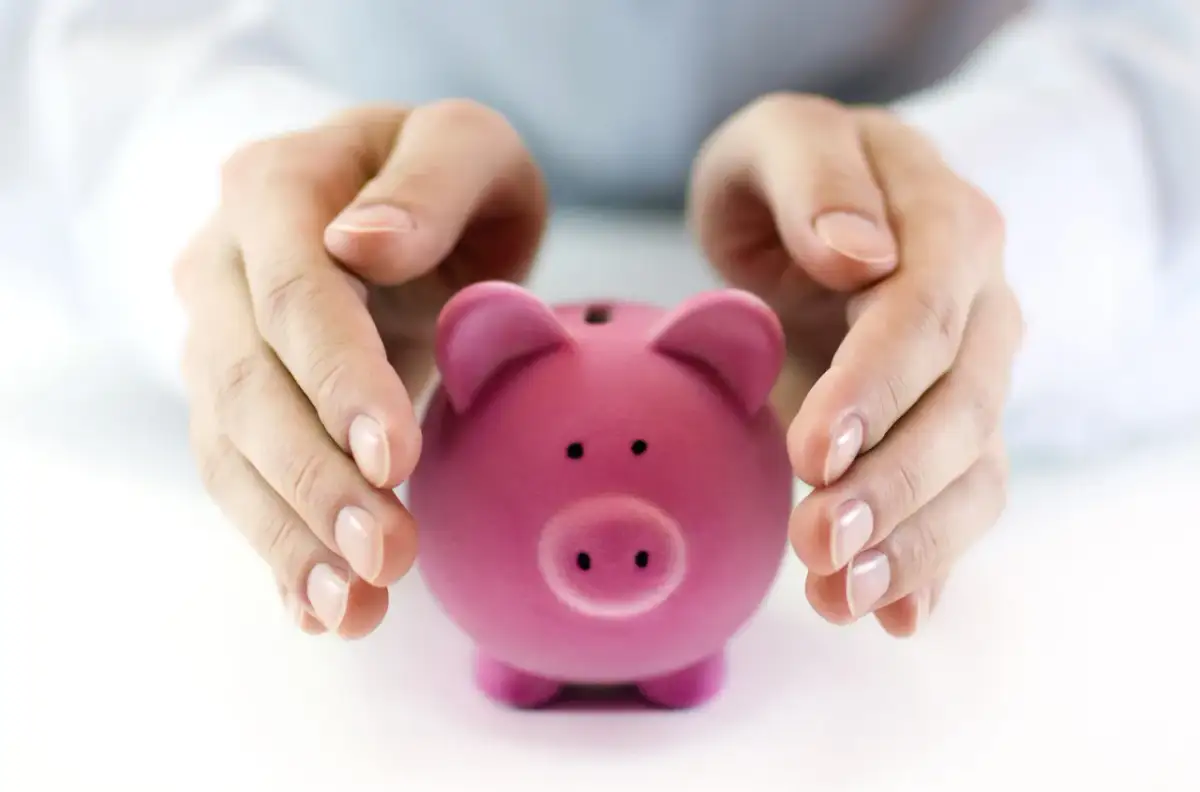 Różowa świnka-skarbonka pod dłońmi. Zastanawiasz się, ile wynosi składka na fundusz pracy?