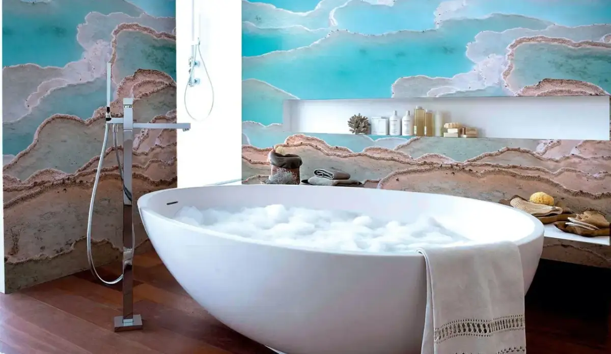 Wanna z pianą i prysznic w łazience z tapetą imitującą formacje skalne.