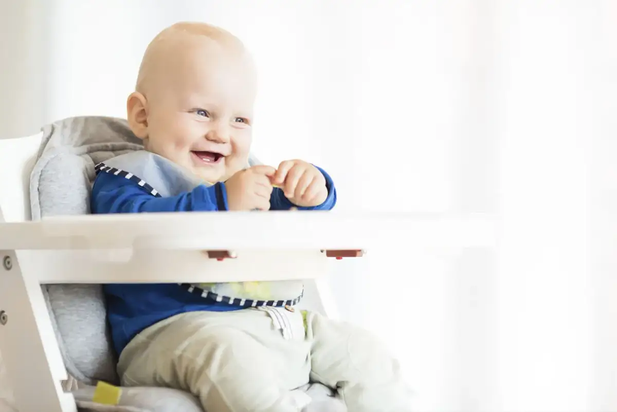 Uśmiechnięty niemowlak w krzesełku, gotowy na pyszny kefir dla niemowlaka.