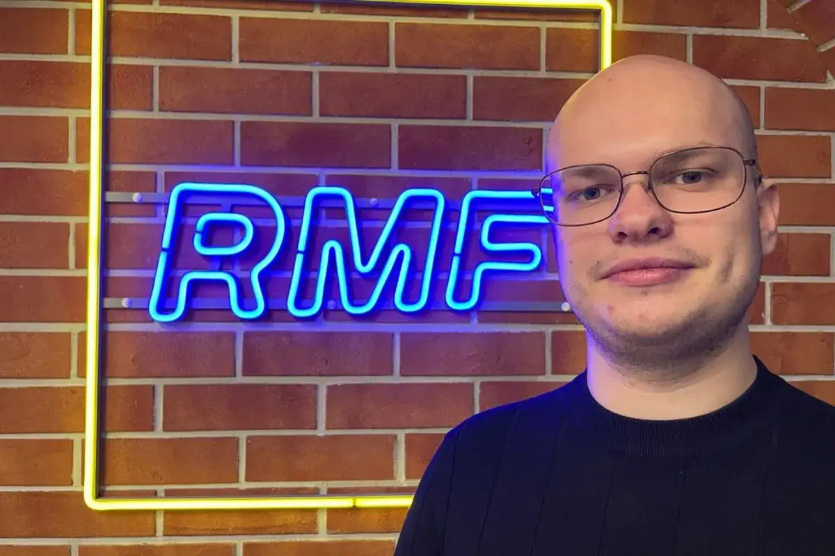 Mężczyzna w okularach stoi przed neonowym napisem RMF FM. Ile jest sejfów w RMF FM? Tego nie wiemy, ale na pewno jest tu dużo dobrej muzyki!