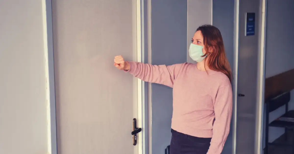 Kobieta w maseczce puka do drzwi gabinetu. Zastanawia się, czy do ginekologa potrzeba skierowania.