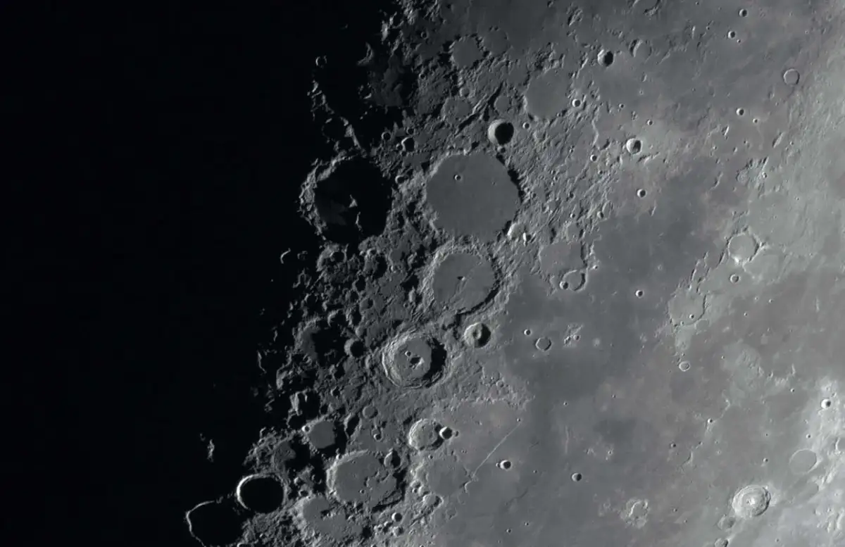 Zbliżenie na powierzchnię Księżyca z licznymi kraterami i cieniami.