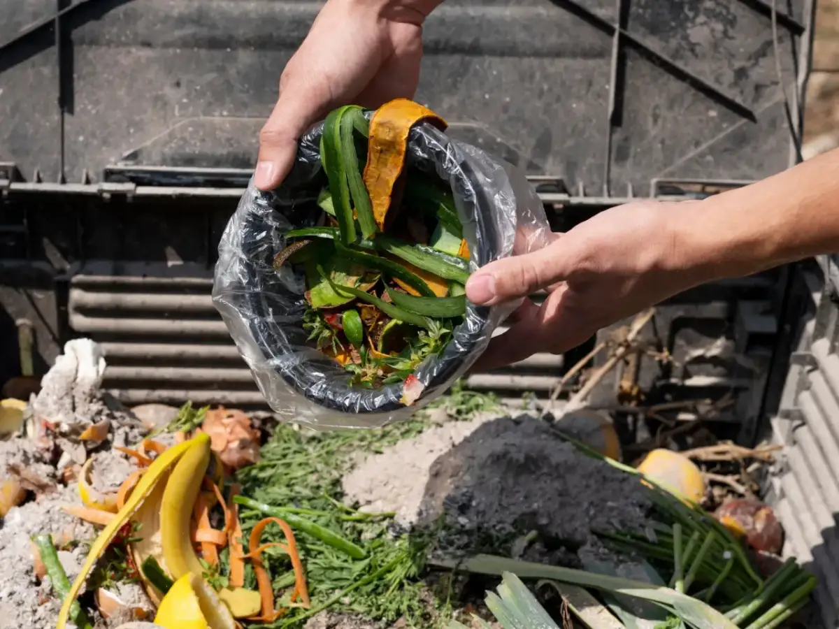 Ręce wsypują do kompostownika resztki roślinne, tworząc cenny nawóz organiczny z odpadów roślinnych.
