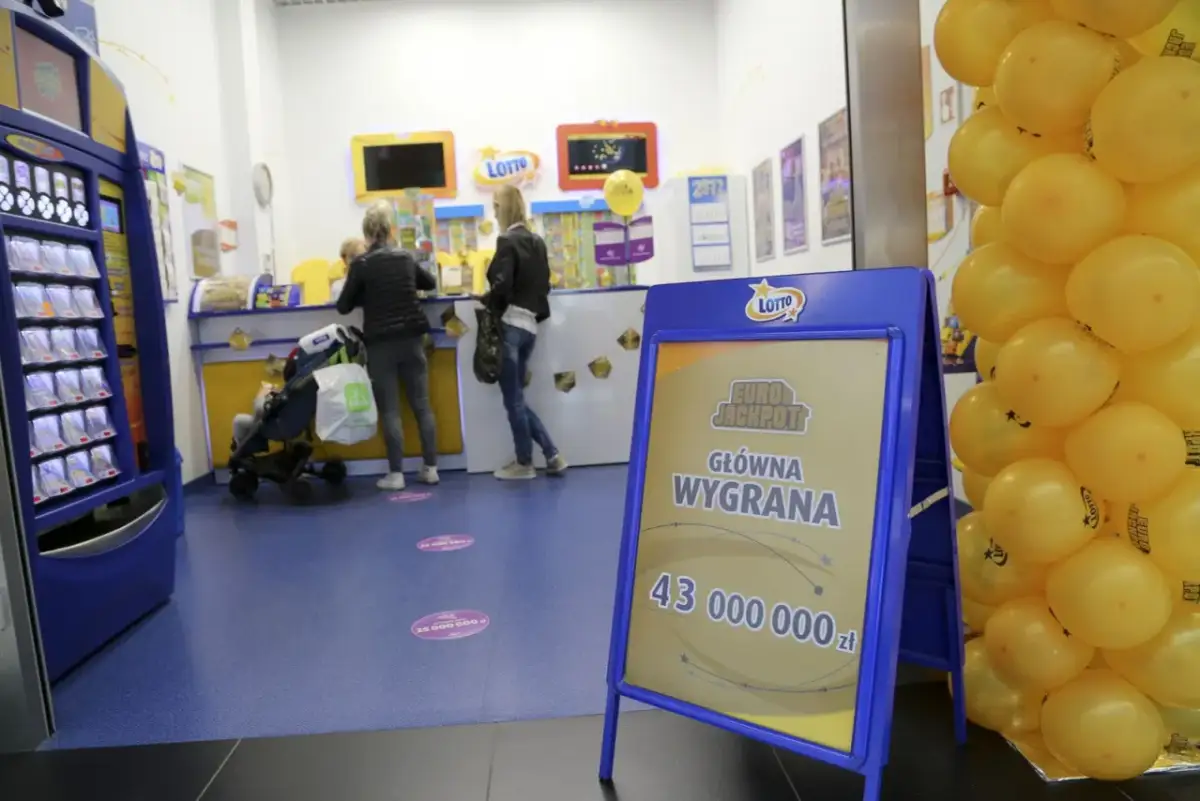 Tablica informacyjna Eurojackpot z kwotą wygranej i żółte balony w punkcie Lotto.