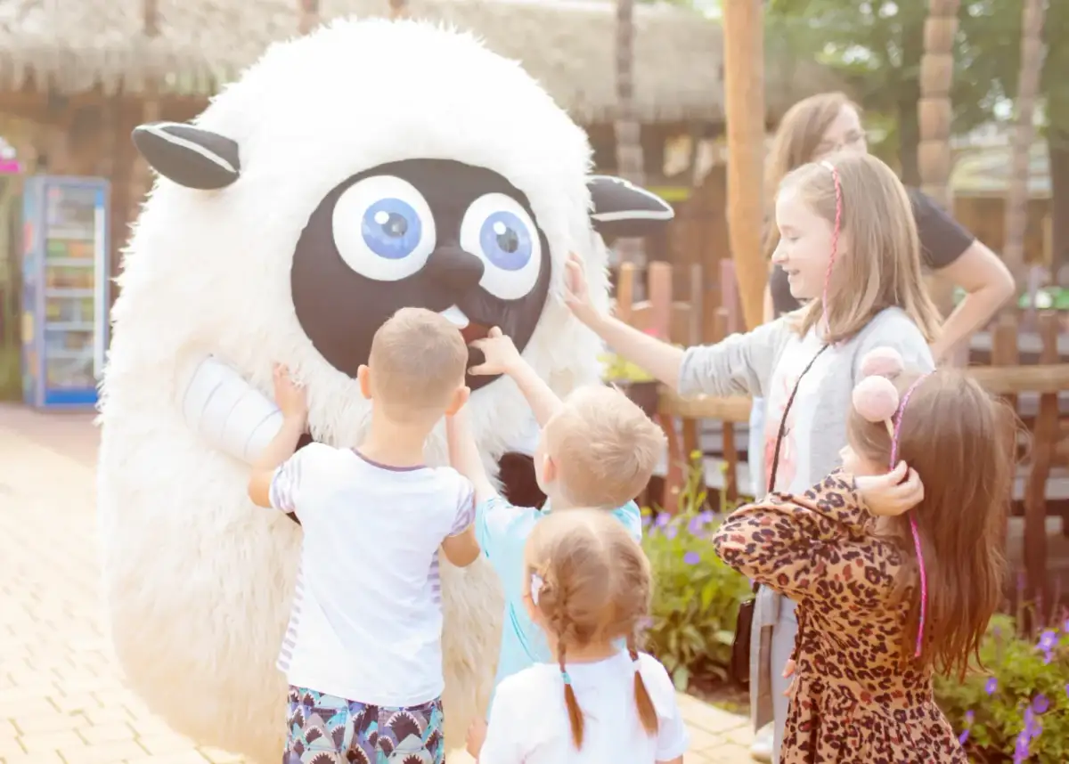 Dzieci dotykają pluszowej postaci owcy w parku rozrywki.
